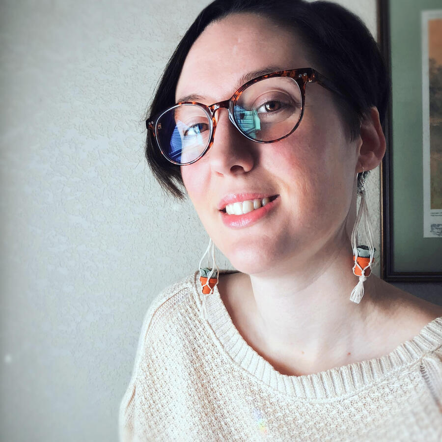 A color photo of the author, Jules Arbeaux, who is wearing glasses and macrame plant earrings.
